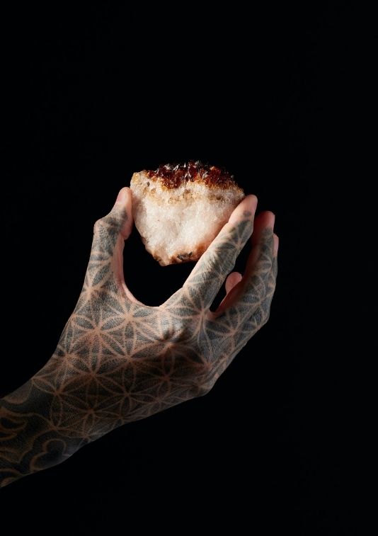 This is a photo of a crystal held in a sacred geometry tattooed hand